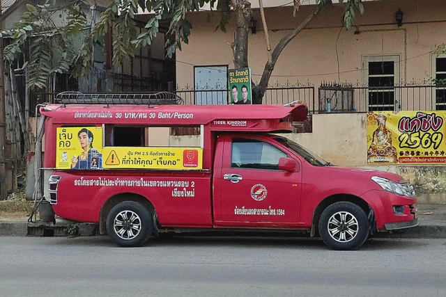 Red songthaew shared taxi driving along a Chiang Mai street