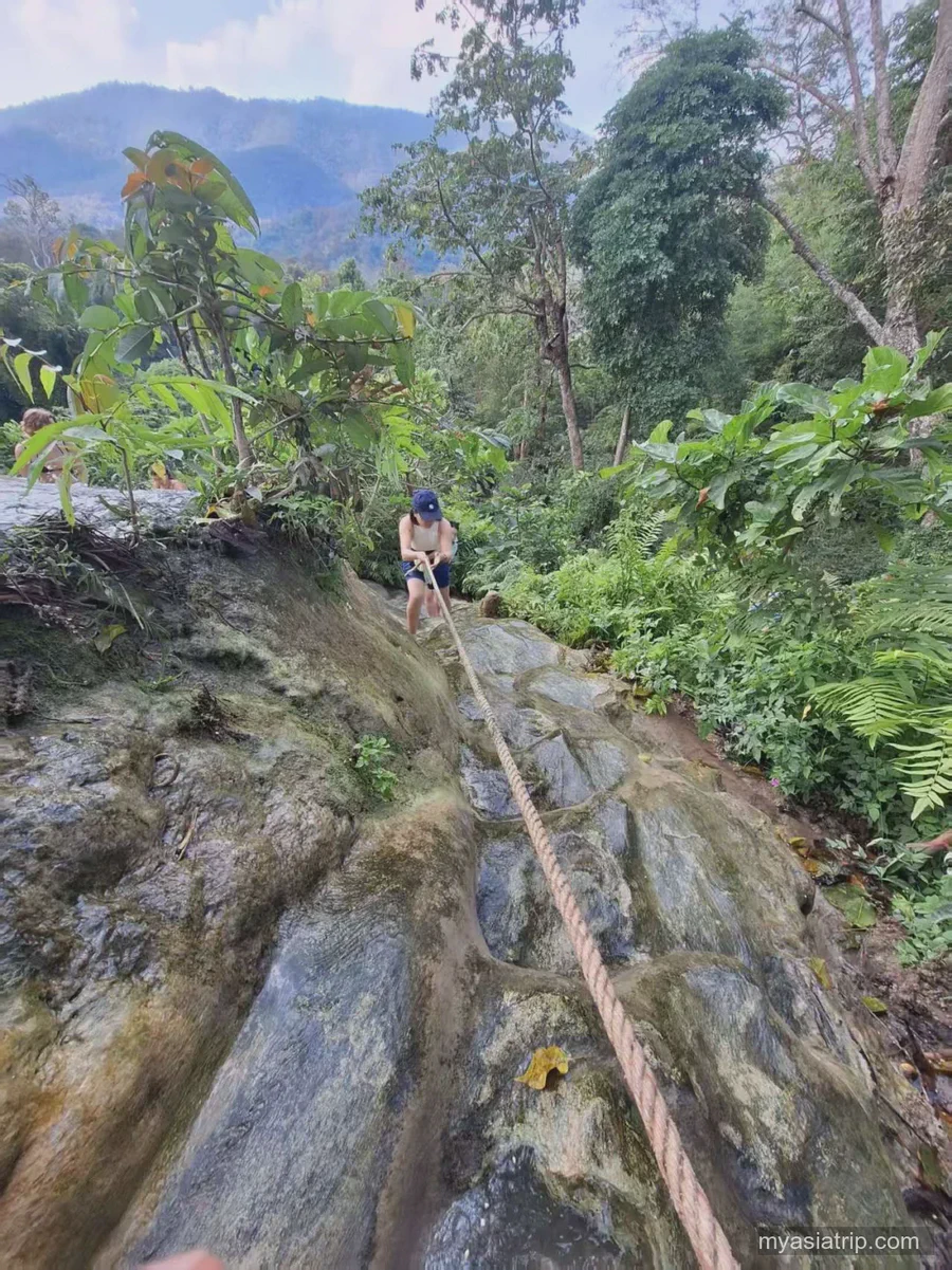 Traveler using a fixed rope on a steep wet section of Bua Tong Sticky Waterfall