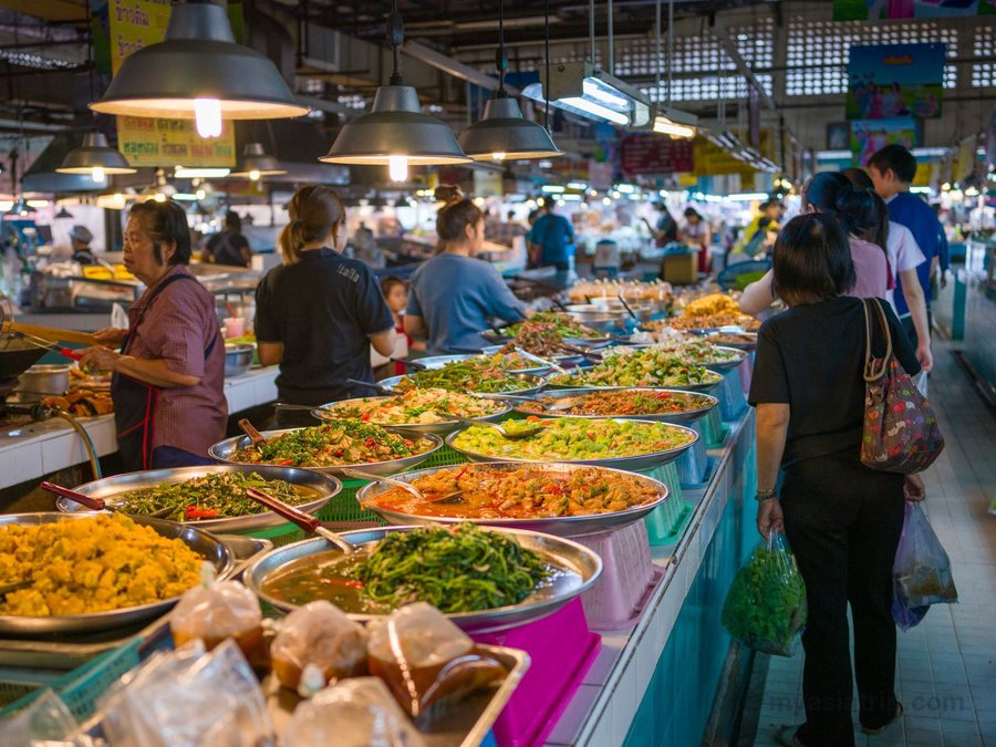 Prepared curries and vegetables displayed in trays at a Thai food market